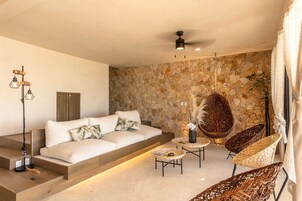 Ein modernes Wohnzimmer mit Steinwand, einer Couch, Korbstühlen und einem Deckenventilator.