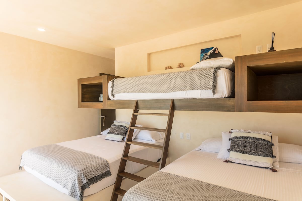 Habitación con literas, una escalera, dos camas y un estante sobre la litera superior.