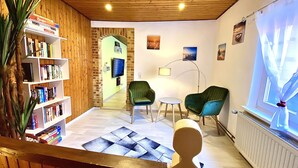 Una sala de estar acogedora con una estantería, dos sillones verdes, una mesita y un televisor.
