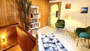Un interior de madera con una estantería, sillas verdes, una pequeña mesa y una escalera.