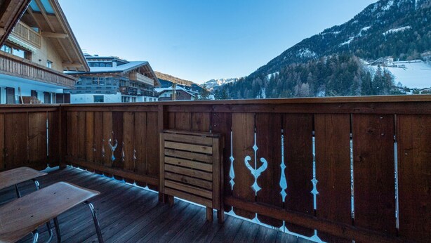 A wooden deck with a table and benches, overlooking a mountainous landscape with buildings in the background. - Apartments Agave 169A (Ortisei)