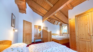 A bedroom with two beds, wooden ceiling beams, and a large wardrobe. - Apartments Agave 169A (Ortisei)