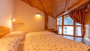 A room with two beds, wooden ceiling beams, a window with curtains, and a wall-mounted light fixture. - Apartments Agave 169B (Ortisei)