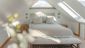 A bedroom with a sloped ceiling, a bed with a floral bedspread, and two bedside tables. - Hillview Hideaway - sleeps 2 guests in 1 bedroom (Gotherington)