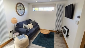 A living room with a sofa, ottoman, round coffee table, and a wall-mounted clock.