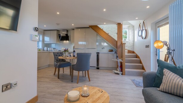 A modern living room with a sofa, a coffee table with candles, and a staircase leading to a kitchen area. - Hillview Hideaway - sleeps 2 guests in 1 bedroom (Gotherington)