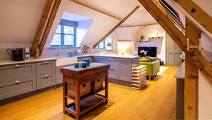 Eine moderne Loft-Küche mit Holztisch, grauen Schränken und Blick ins Freie durch ein großes Fenster.