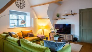 A cozy living room with a green sofa, a TV, a lamp, and a clock on the wall.