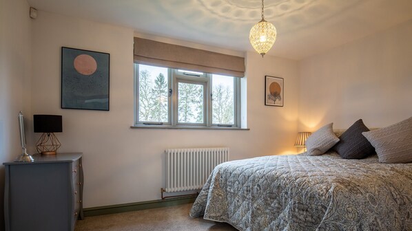 Una camera da letto con un letto, un termosifone, una finestra con persiane, una lampada e un quadro appeso al muro.