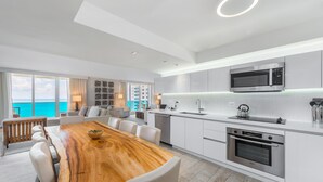 Une cuisine moderne avec une table à manger en bois, des meubles blancs et une vue sur l’océan.