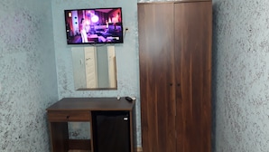 Ett rum med en garderob i trä, ett litet skrivbord med en dator, en väggmonterad TV och en luftkonditioneringsanläggning.