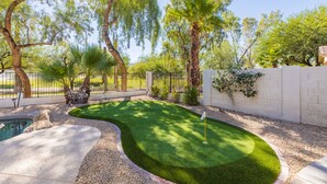 Ein Garten mit Putting-Grün, Pool und einer Steinmauer.