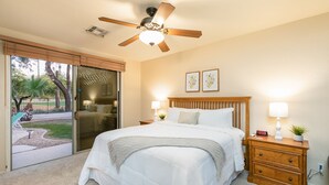 Ein Schlafzimmer mit Bett, Nachttisch, Deckenventilator und Blick ins Freie.