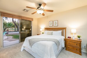 Relax in this serene bedroom with a large bed, nightstand, and ceiling fan, offering a peaceful retreat with a patio and outdoor views.