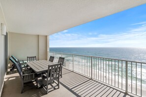 A balcony with a table and chairs, overlooking a beach with waves. - Beautiful Beachfront Condo with Amazing Views and Beachfront Pool! Chair Service Included* (Panama City Beach)