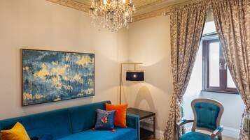 Una habitación con un sofá azul, una silla decorativa, una araña y un cuadro abstracto grande.