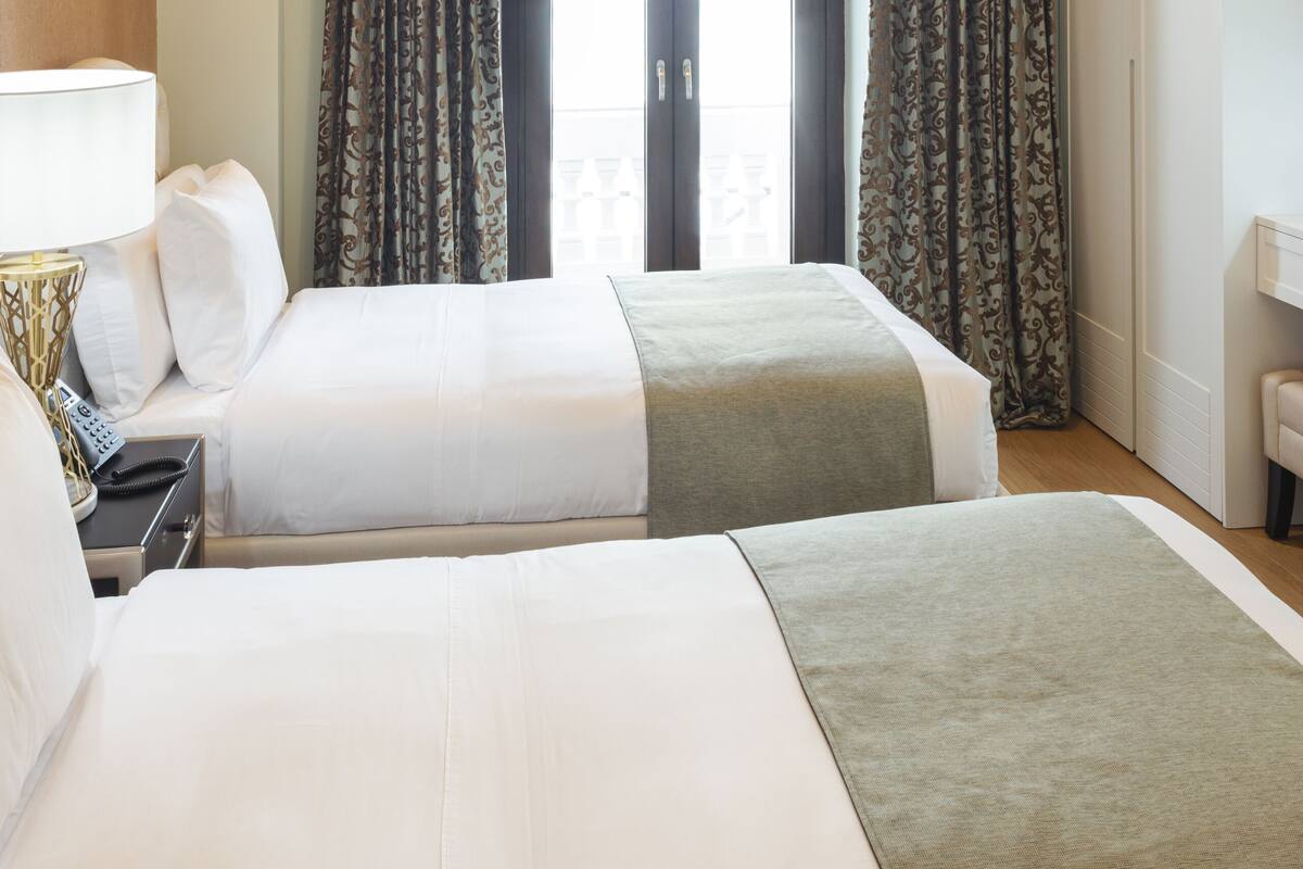 Hotellihuone, jossa on kaksi sänkyä, kattokruunu ja suuri ikkuna, jossa on verhot.