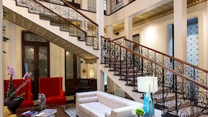 Un hall d’entrée spacieux, avec un fauteuil rouge, un canapé blanc, une table basse en bois et un escalier orné de rampes noires.