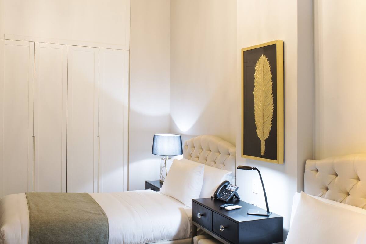 Hotellihuone, jossa on kattokruunu, sänky, yöpöytä ja seinälle ripustettu taideteos.