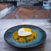 Plato de comida con un huevo pochado encima, decorado con microhojas, sobre un plato azul.