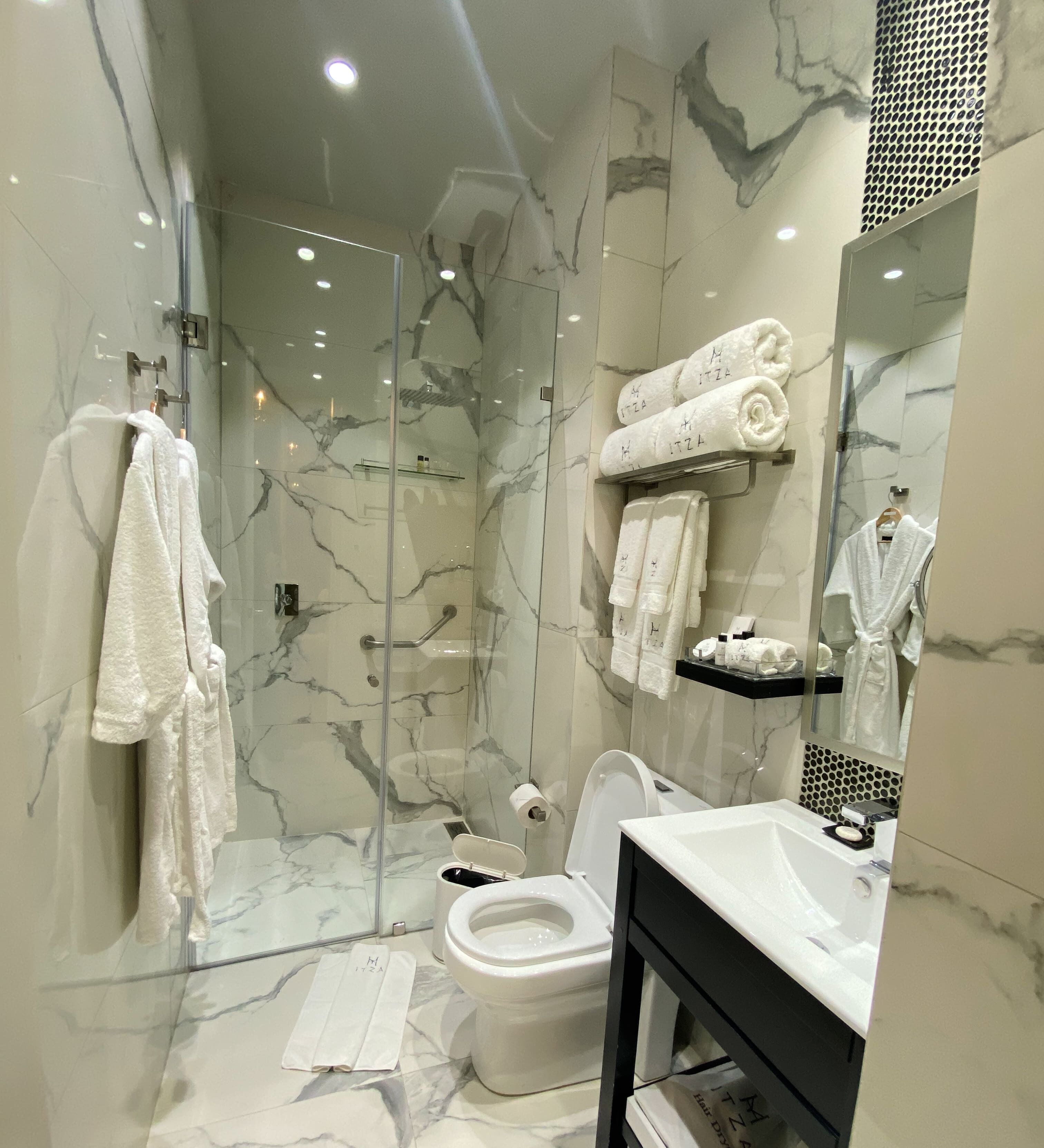 A modern bathroom with a glass-enclosed shower, marble walls, and a white sink with a black vanity.