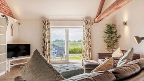 A living room with a leather sofa, a flat-screen TV, and a sliding glass door leading to a patio. - 1 bedroom accommodation in Ocle Pychard (Ocle Pychard)