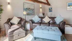 A modern living room with leather sofas, a light blue ottoman, and wooden beams on the ceiling. - 1 bedroom accommodation in Ocle Pychard (Ocle Pychard)