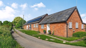 A brick house with a sloped roof, solar panels, and a gravel driveway. - 1 bedroom accommodation in Ocle Pychard (Ocle Pychard)