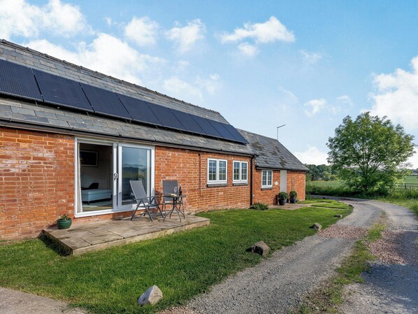 A brick house with solar panels on the roof, a patio with chairs, and a gravel path. - 1 bedroom accommodation in Ocle Pychard (Ocle Pychard)