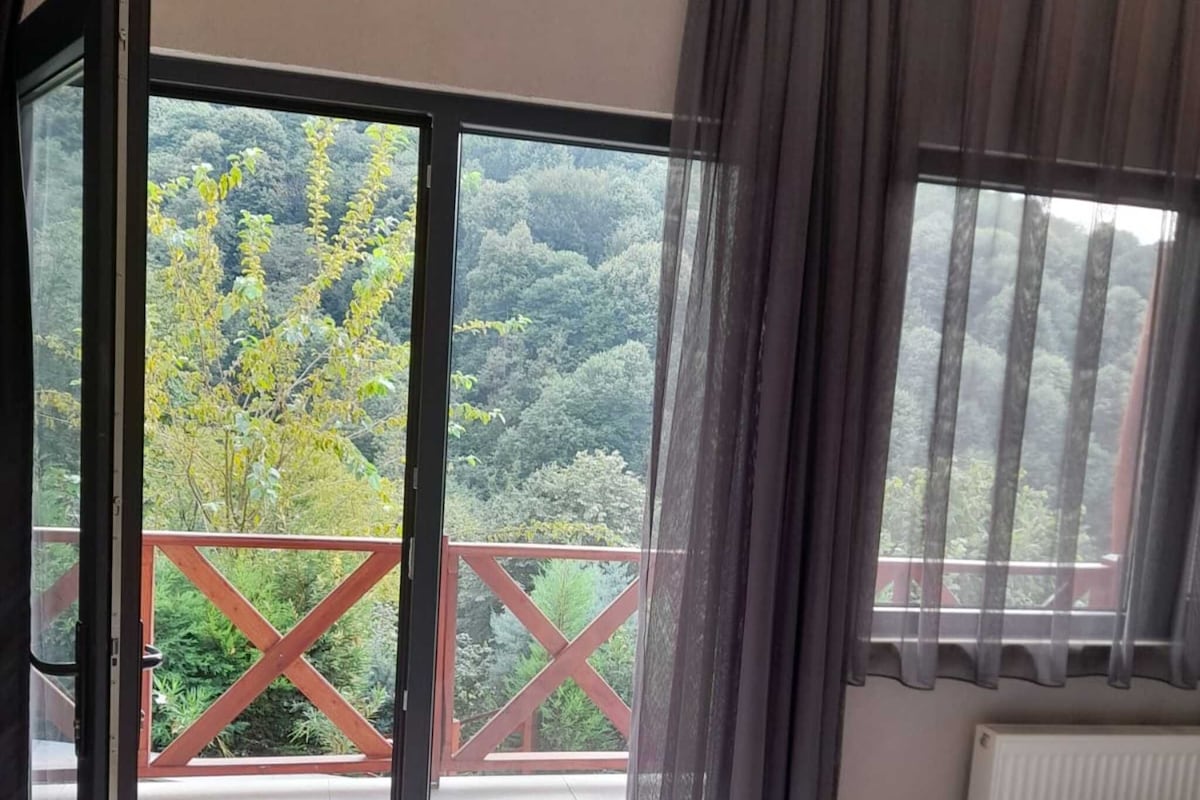 Quarto com cama, janela com cortinas, vista para uma varanda e porta que dá para o exterior.
