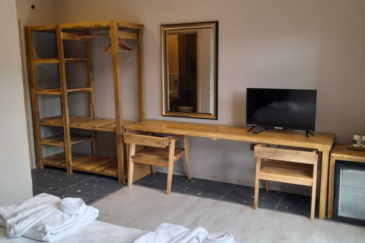 Une chambre d’hôtel avec un lit, un bureau en bois, une télévision et un miroir.