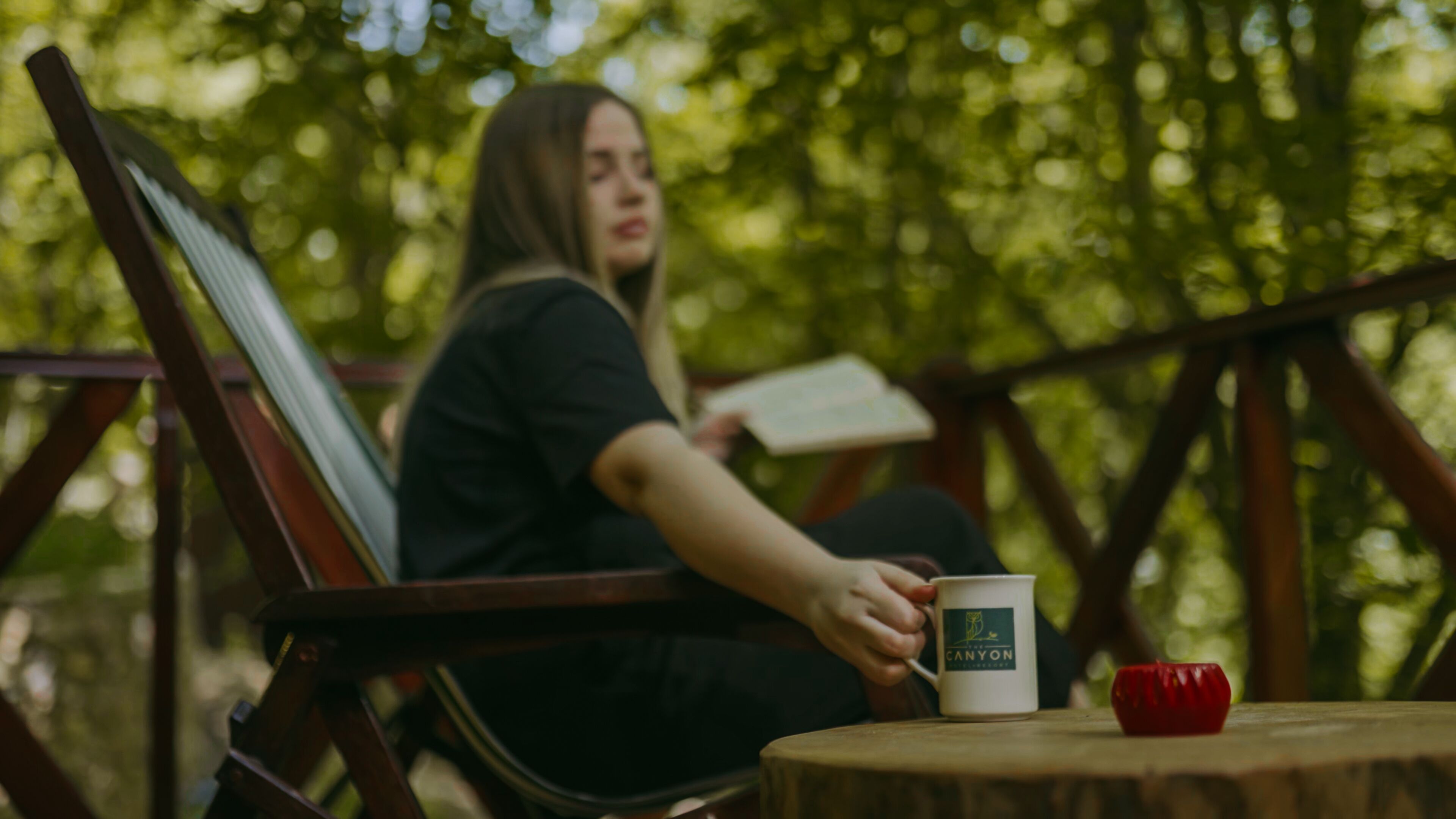 A person sitting on a wooden bench outdoors, holding a book.