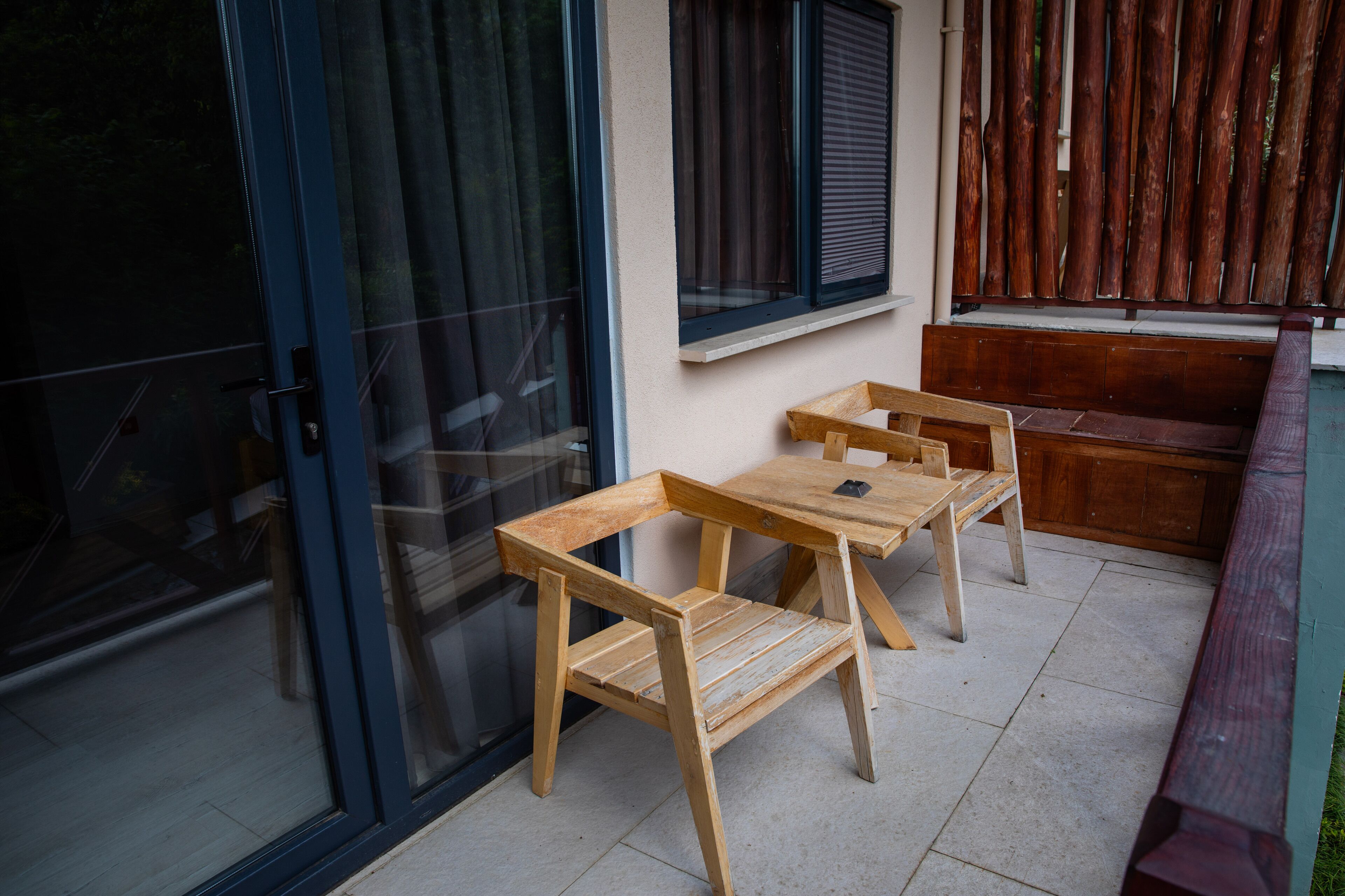A patio with two wooden tables and chairs, a sliding glass door, and a wooden bench.