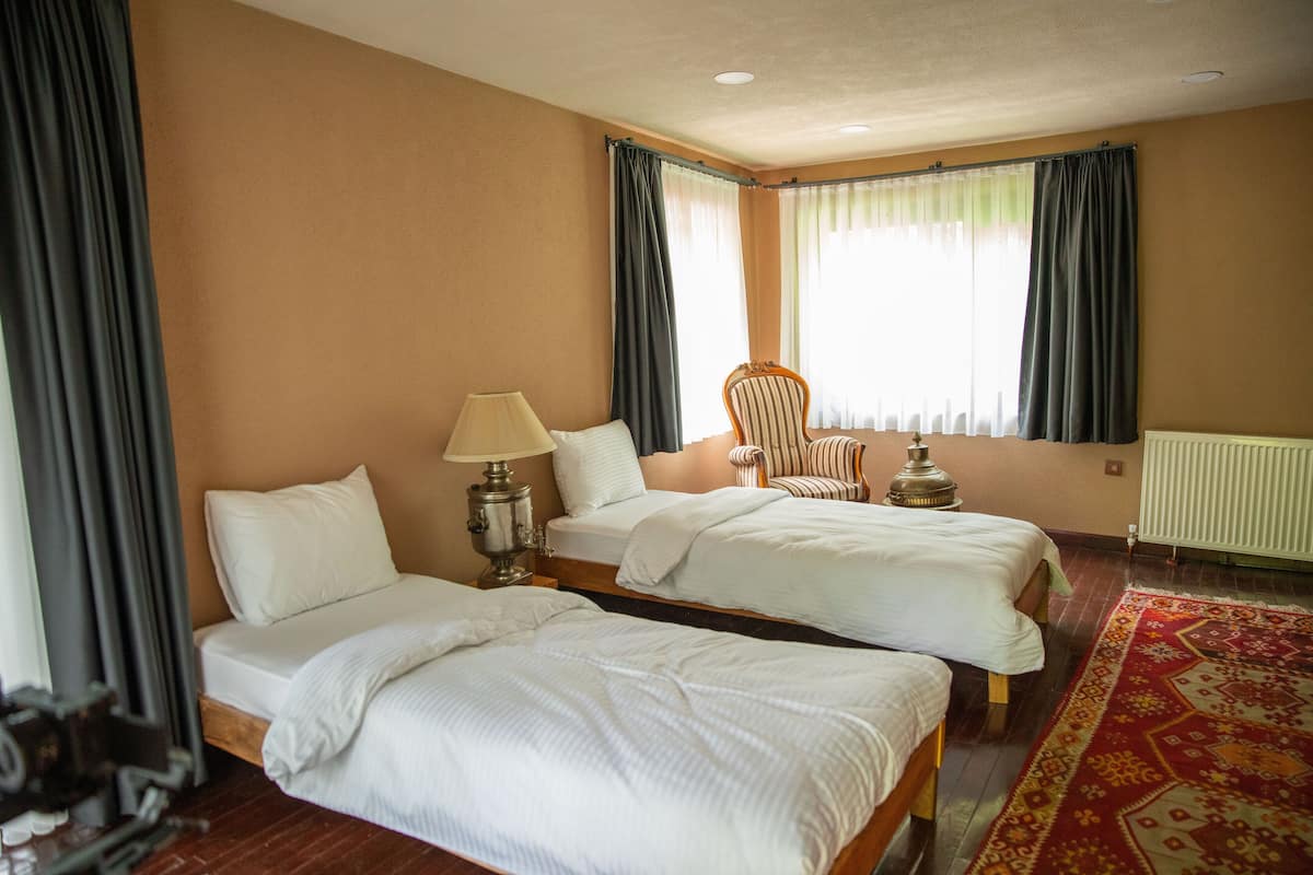 Habitación de hotel con dos camas, una silla, una lámpara y un ventanal con cortinas.