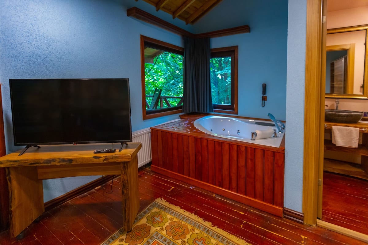 Un baño con una bañera de madera, un espejo grande y un televisor sobre una mesa de madera.