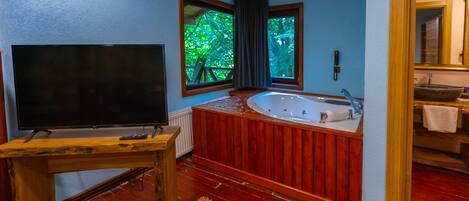 A bathroom with a wooden bathtub, a large mirror, and a television on a wooden table.