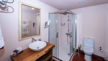 Un baño con tocador de madera, lavamanos blanco, cabina de ducha de vidrio y un inodoro.