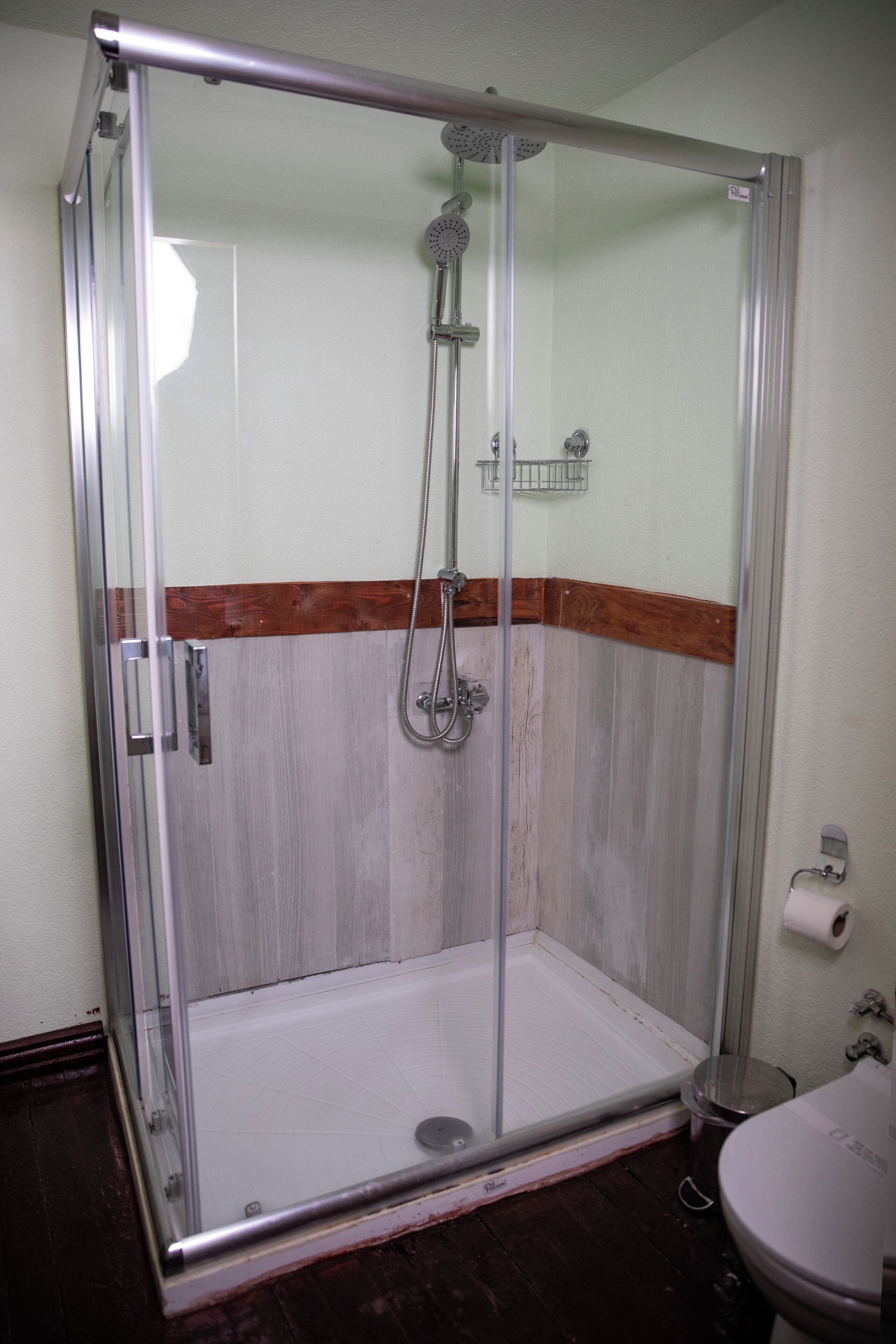 A glass-enclosed shower with a wooden baseboard, a metal showerhead, and a small shelf.