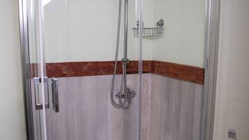 A glass-enclosed shower with a wooden baseboard, a metal showerhead, and a small shelf.