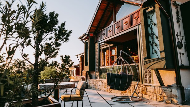 Een modern gebouw met een gevel van natuursteen, grote ramen en een terras met tafels en stoelen.