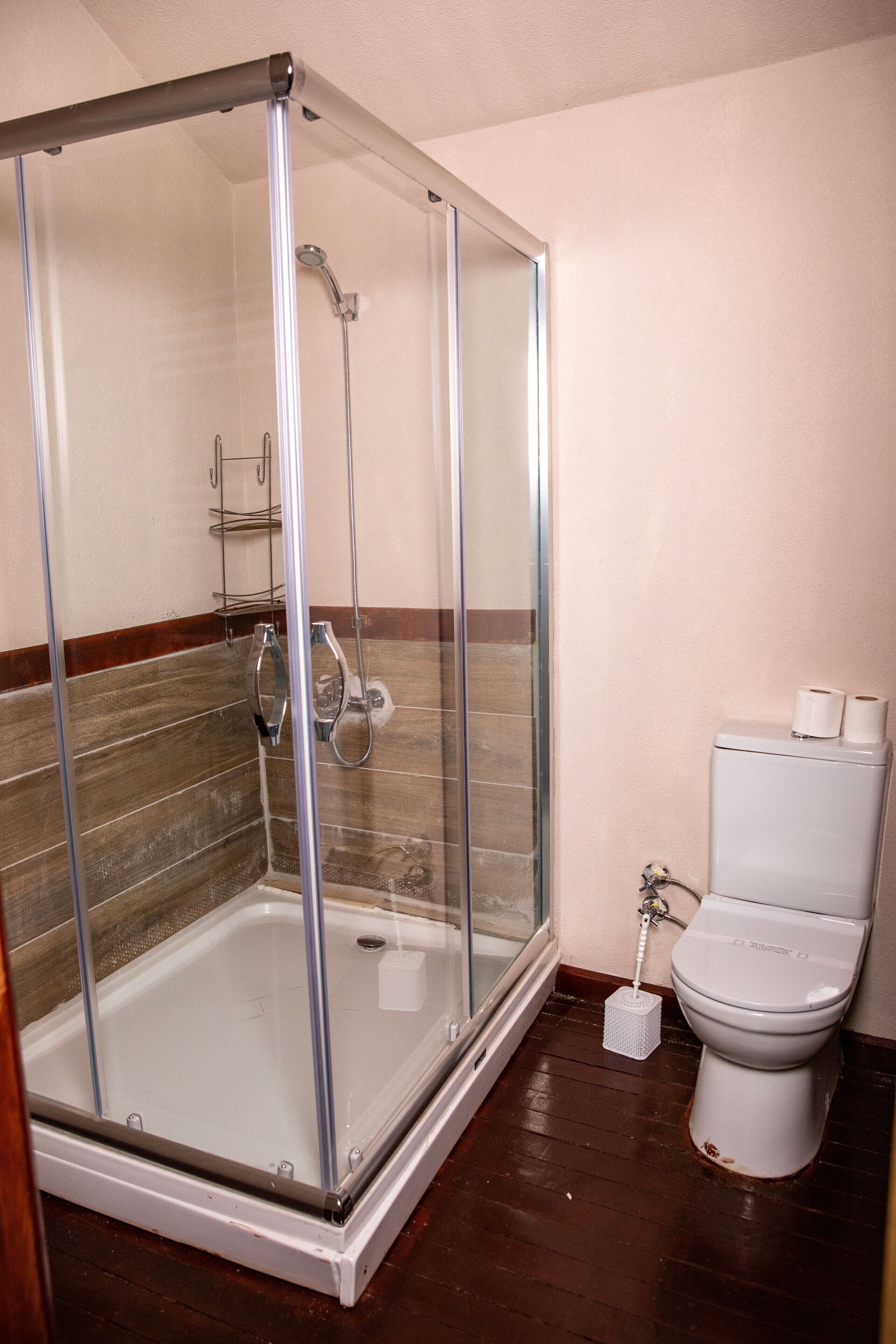 A bathroom with a glass-enclosed shower, a toilet, and a small trash bin.