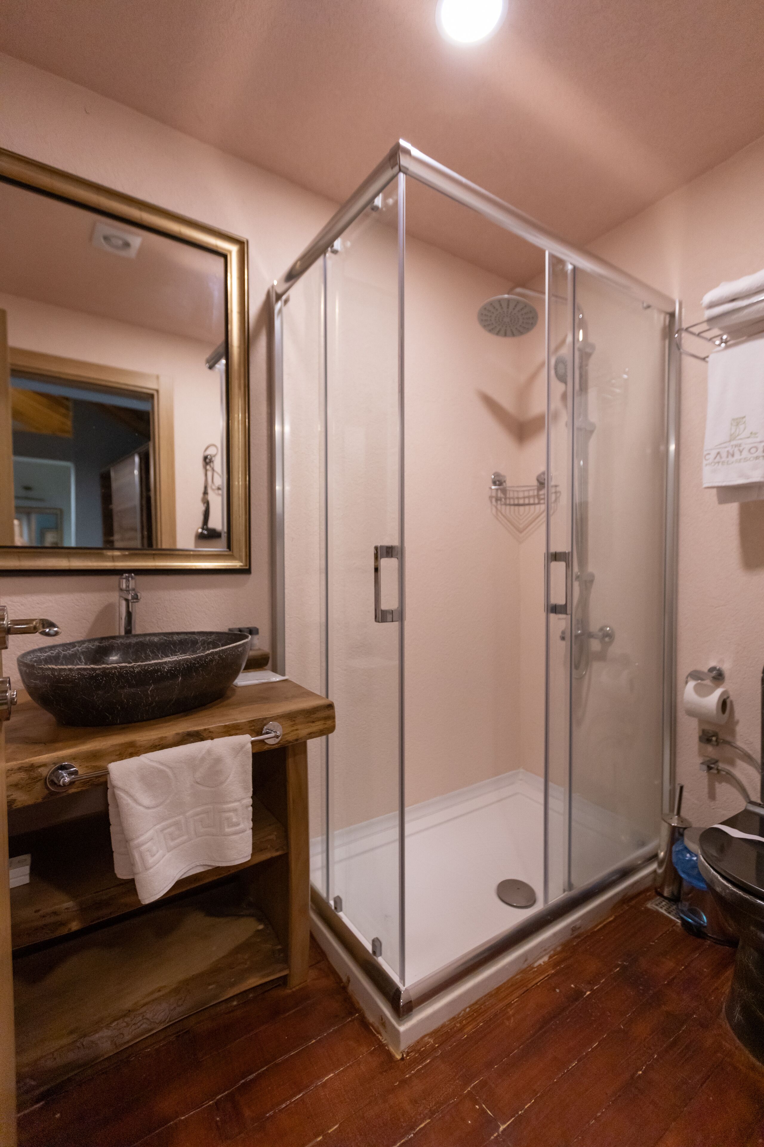 A bathroom with a wooden vanity, a large mirror, a glass-enclosed shower, and a white towel on the counter.