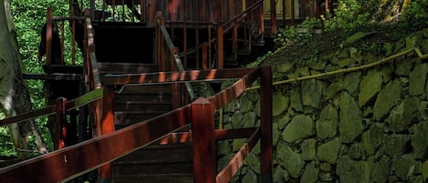 A rustic wooden cabin with a stone wall and wooden staircase leading to a wooden deck.