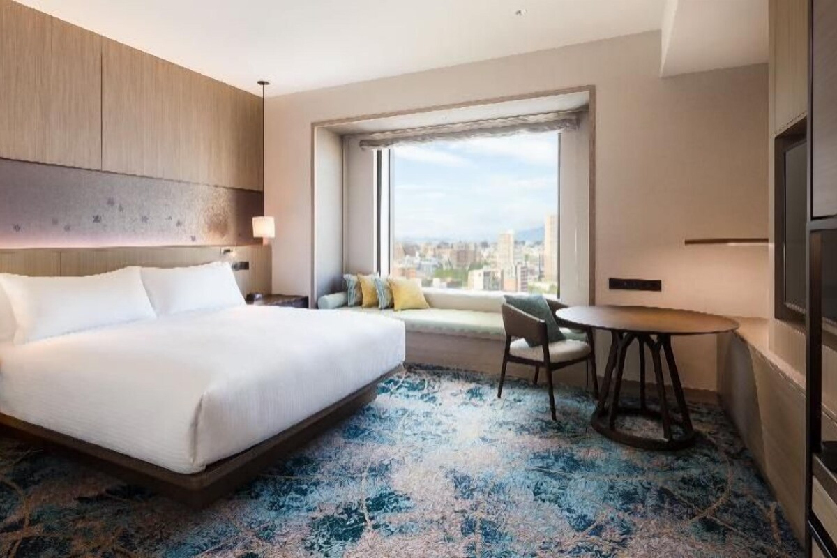 A hotel room with a large bed, a sofa, a small table, and a TV.