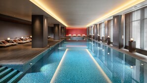 Una piscina interior moderna con superficie de agua cristalina, solárium de madera y zona de descanso con asientos.