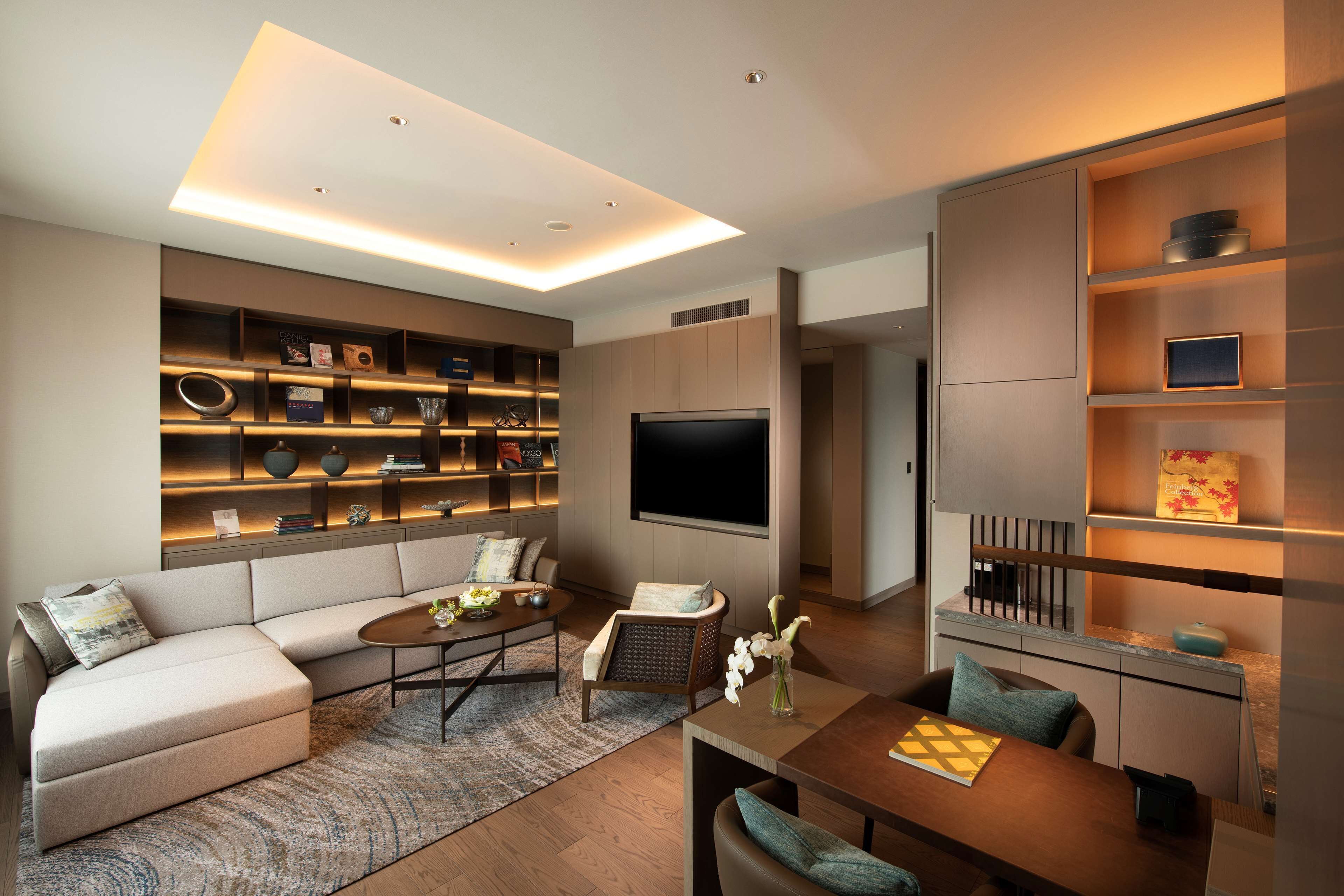 A modern living room with a sectional sofa, a coffee table, a TV, and built-in shelving with decorative items.