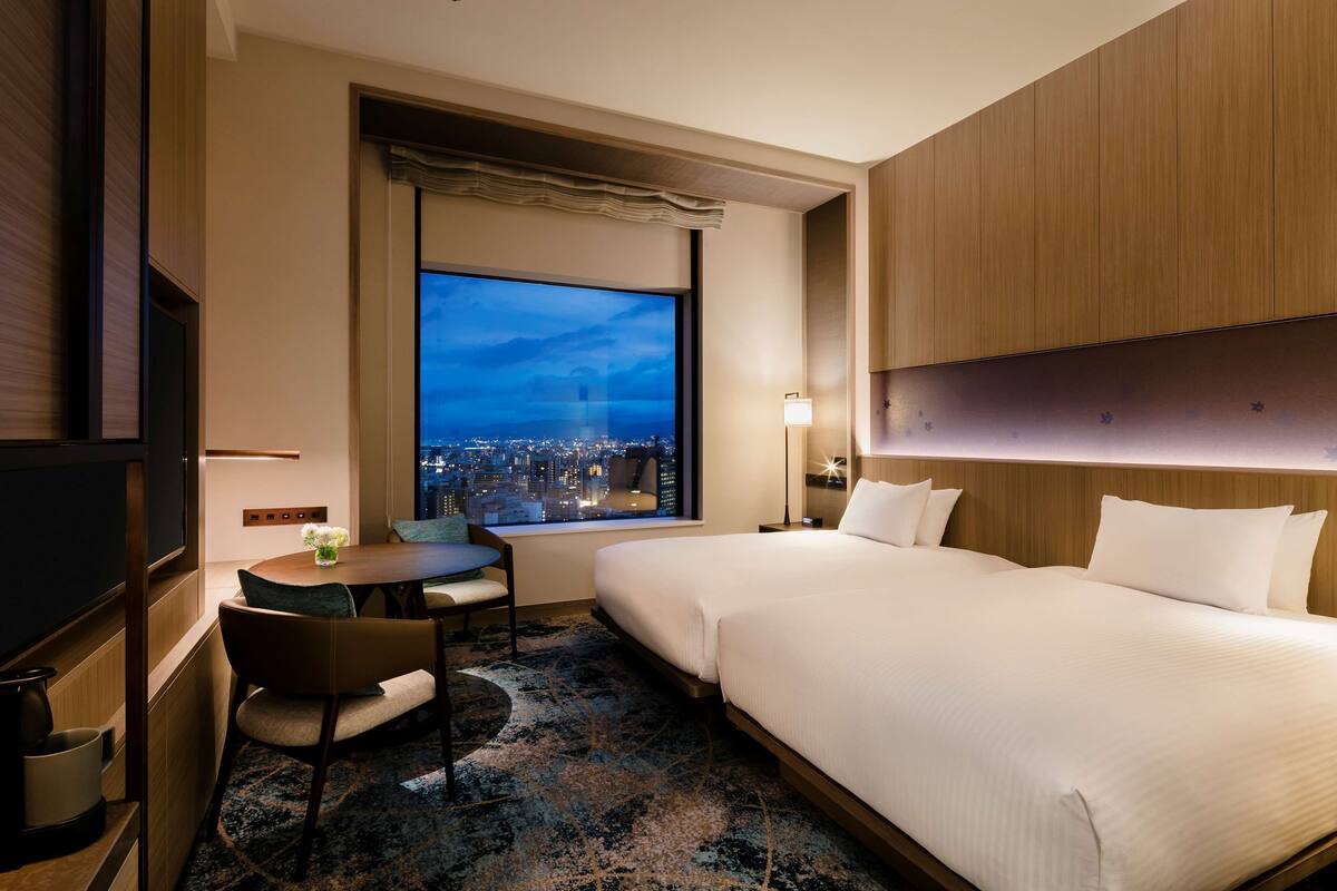 Una habitación de hotel con un ventanal grande, una cama, un escritorio con una silla y un televisor.