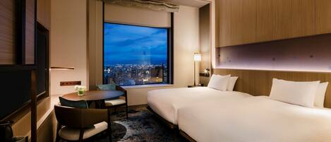 A hotel room with a large window, a bed, a desk with a chair, and a TV.