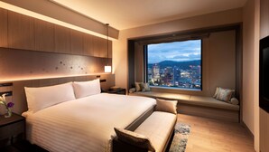 A modern hotel room with a large bed, a seating area with a view of the city, and a large window. - Hilton Hiroshima (Hiroshima)