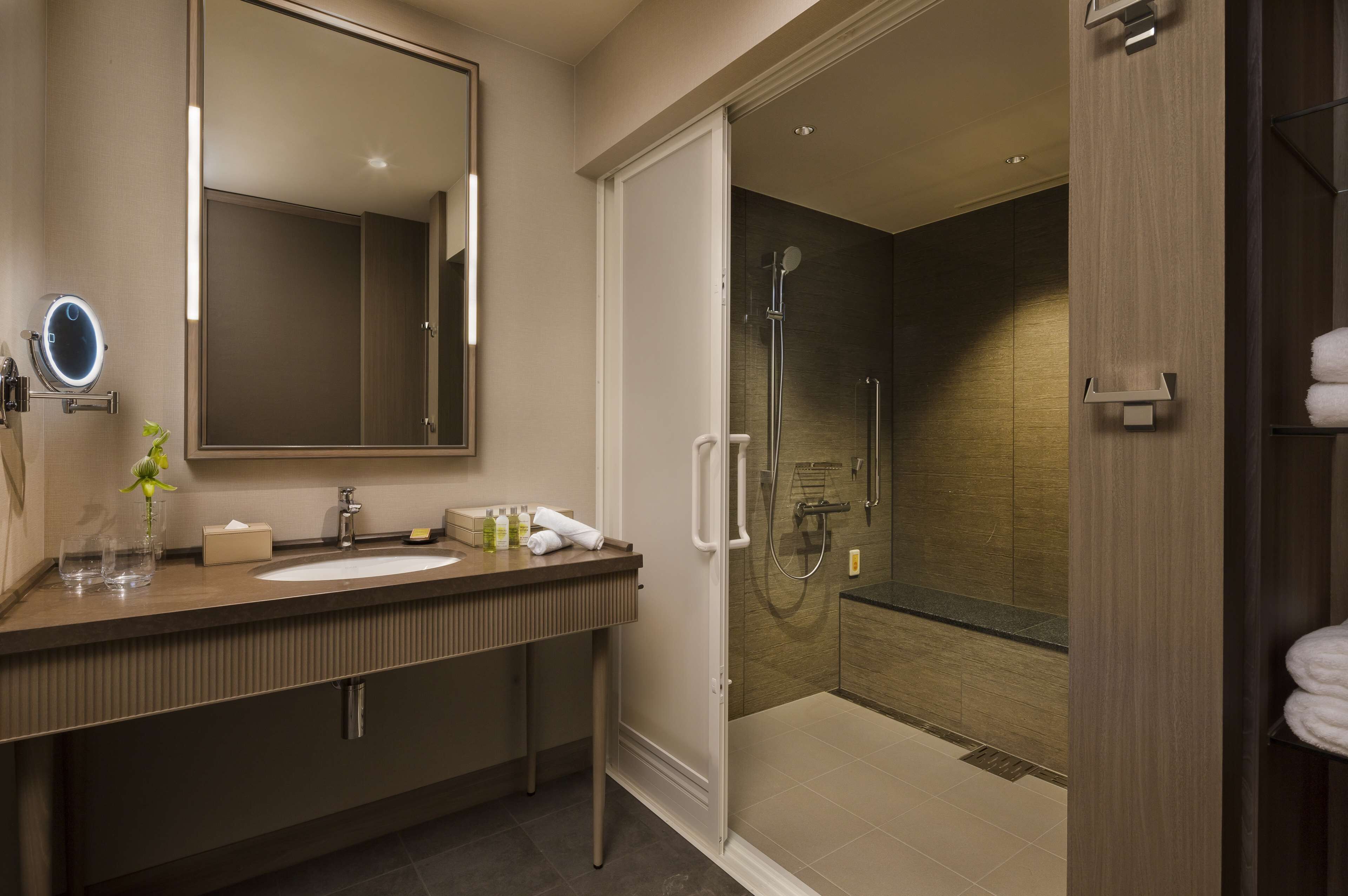 A modern bathroom with a large mirror, a sink, and a walk-in shower.